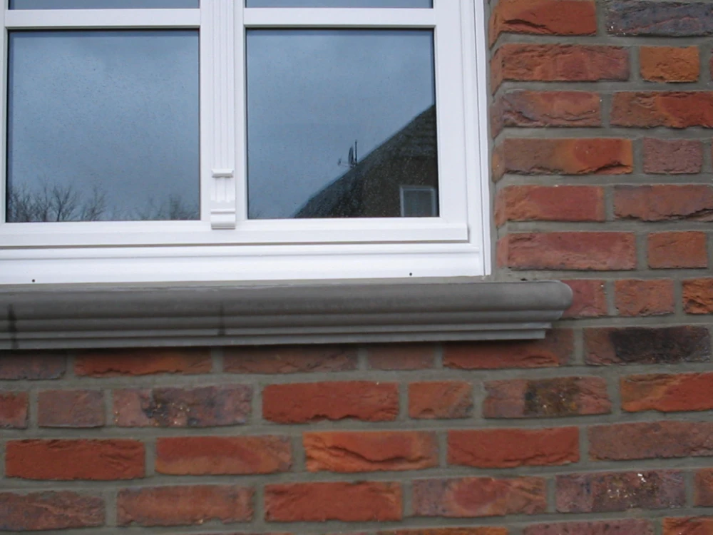 Beton-Fensterbank unter weißem Sprossenfenster in roter Klinkerfassade