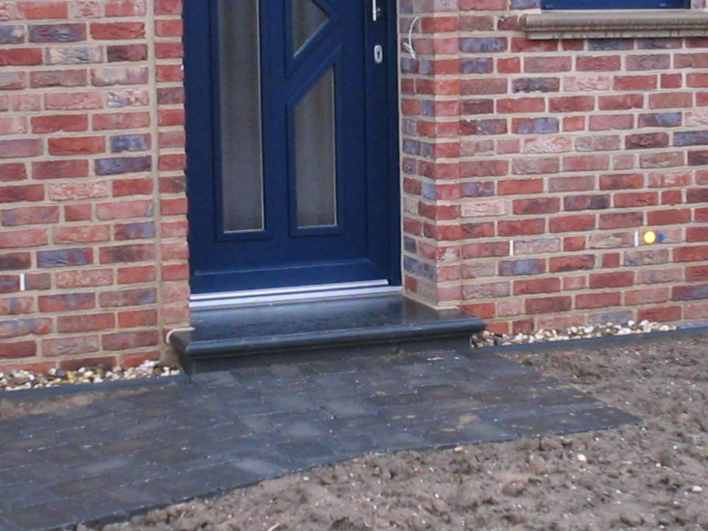 Dunkle Beton-Stufe vor Eingangstür in roter Klinkerfassade