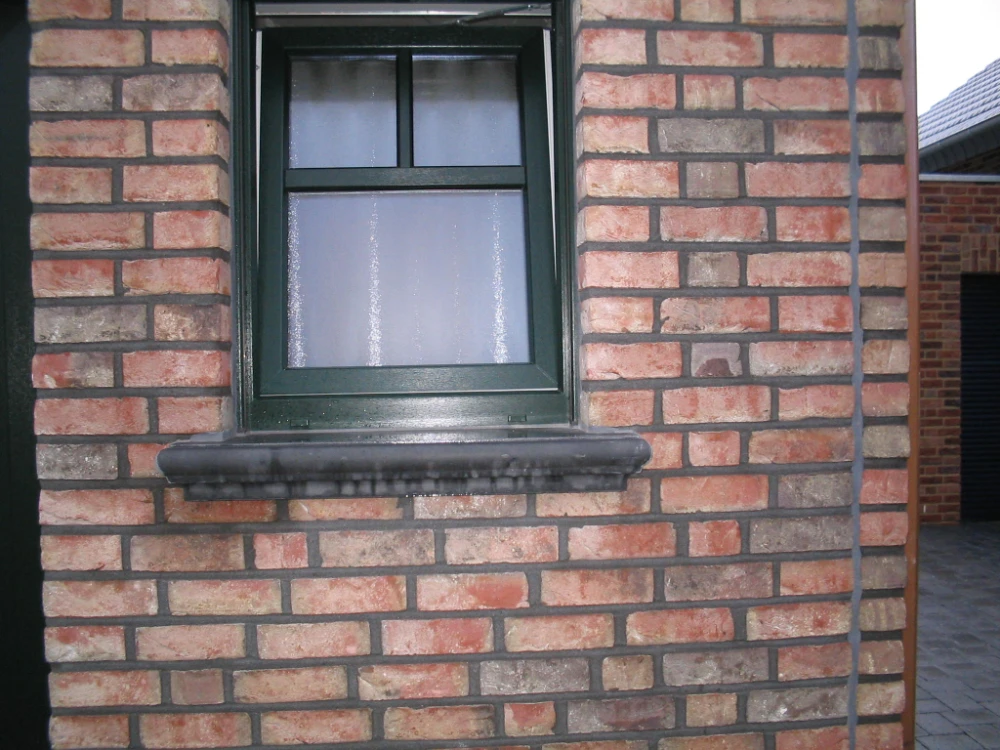 Graue Beton-Fensterbank unter grünem Fenster in rot-grauer Klinkerfassade