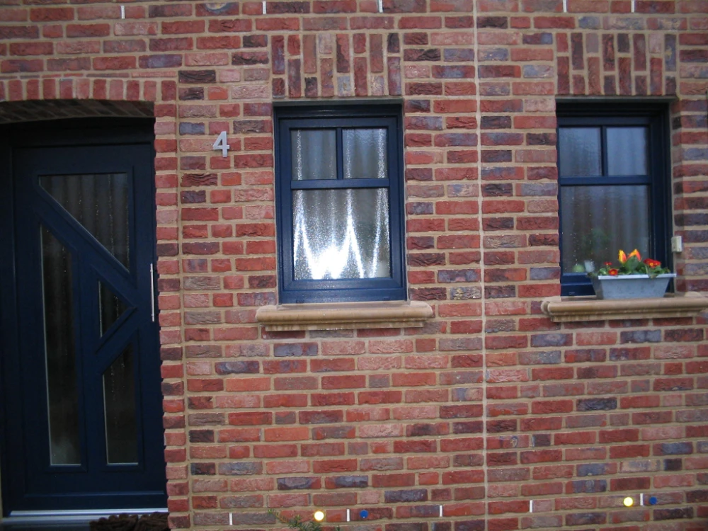 Hausfassade mit dunkelblauer Haustür und zwei Fenstern mit hellen Beton-Fensterbänken