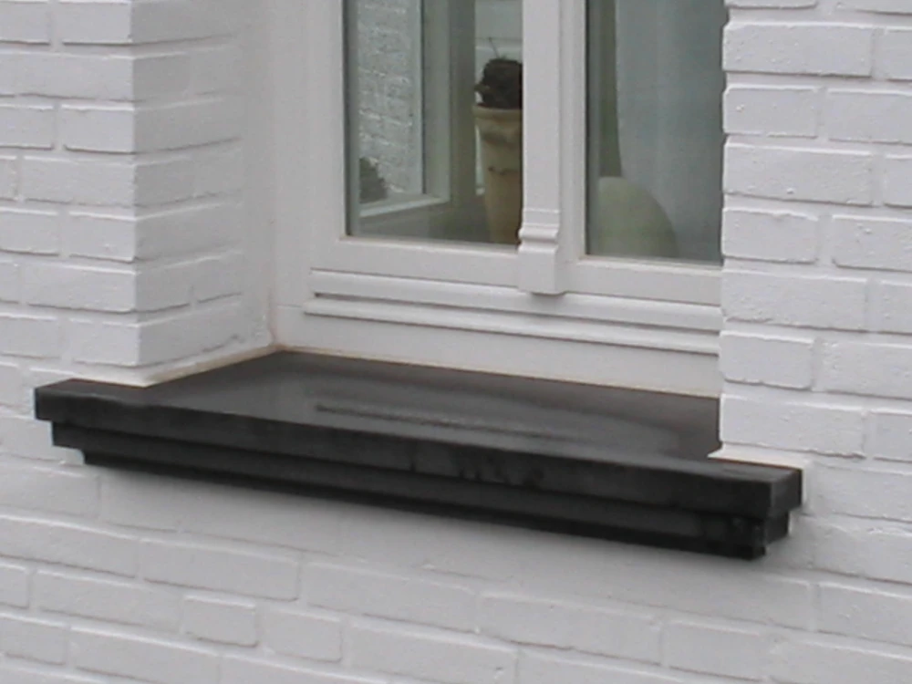 Schwarze Beton-Fensterbank unter weißem Fenster in weiß gestrichener Klinkerfassade