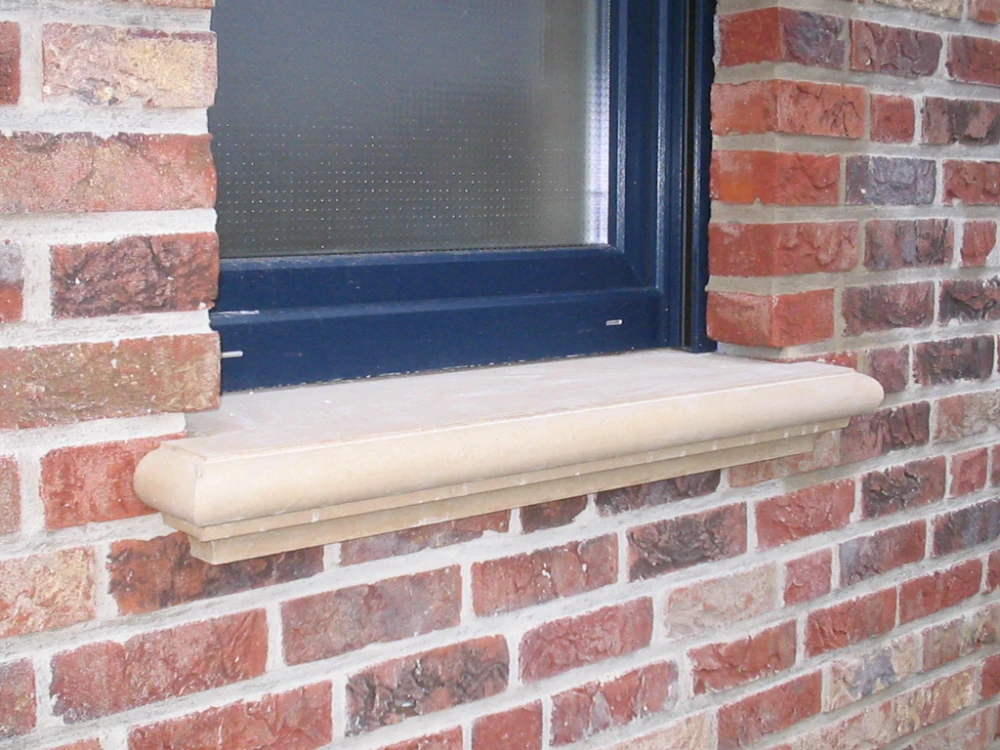 Helle Beton-Fensterbank in Sandfarbe unter dunkelblauem Fenster in Klinkerfassade