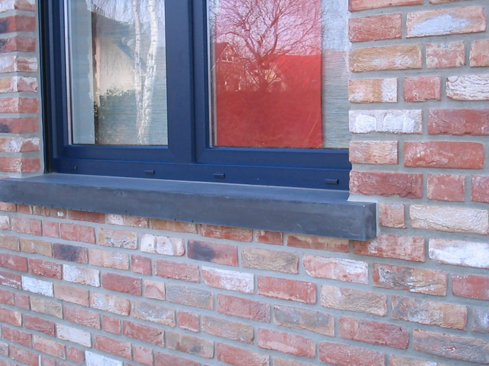 Dunkle Beton-Fensterbank unter dunkelblauem Fenster an gemischter Klinkerfassade