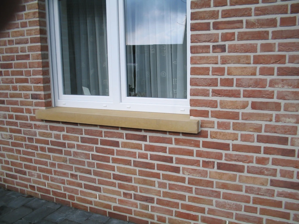 Sandfarbene Beton-Fensterbank unter weißem Fenster in roter Klinkerfassade