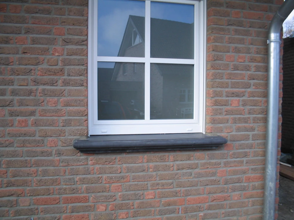 Dunkle Beton-Fensterbank unter weißem Sprossenfenster an brauner Klinkerfassade