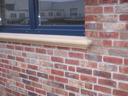 Fensterbank aus Beton Modell 001/1000 an klassischer Ziegelfassade Beton-Fensterbank Modell 001/1000 unter blauem Fenster in roter Klinkerwand
